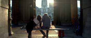 Movie still from “3 Days to Kill” (2014), directed by McG – A man and a woman sitting on a bench in front of a building; Wide shot, Low angle
