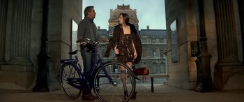 Movie still from “3 Days to Kill” (2014), directed by McG – A man and a woman standing next to a bicycle; Wide shot, Low angle