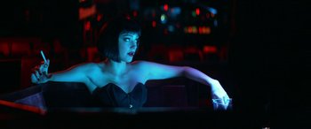 Movie still from “3 Days to Kill” (2014), directed by McG – A woman sitting at a table in front of lights; Medium shot, Low angle