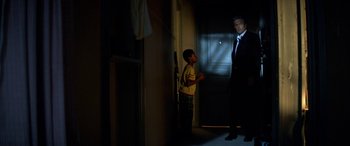 Movie still from “3 Days to Kill” (2014), directed by McG – A man in a suit standing next to a door; Wide shot, Over the shoulder angle