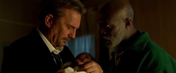 Movie still from “3 Days to Kill” (2014), directed by McG – A man and a man holding a baby in a room; Close Up shot, Low angle