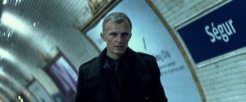 Movie still from “3 Days to Kill” (2014), directed by McG – A man in a black jacket standing next to a wall; Close Up shot, Low angle