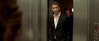 Movie still from “3 Days to Kill” (2014), directed by McG – A man in a suit and tie standing in front of a door; Medium shot, Low angle