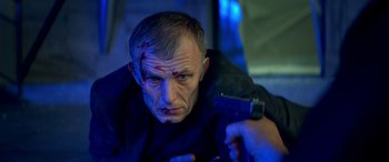 Movie still from “3 Days to Kill” (2014), directed by McG – A man in a black shirt is holding a gun; Close Up shot, Low angle