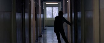 Movie still from “4 Months, 3 Weeks and 2 Days” (2007), directed by Cristian Mungiu – A person standing in a dark hallway near a window; Wide shot, Low angle