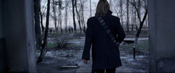 Movie still from “4 Months, 3 Weeks and 2 Days” (2007), directed by Cristian Mungiu – A person walking in a wooded area holding a bag; Medium shot, Over the shoulder angle