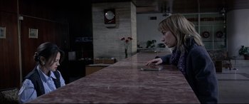 Movie still from “4 Months, 3 Weeks and 2 Days” (2007), directed by Cristian Mungiu – A woman sitting at a counter looking at a cell phone; Medium shot, High angle