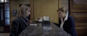 Movie still from “4 Months, 3 Weeks and 2 Days” (2007), directed by Cristian Mungiu – Two women are sitting at a table and one of the women is holding a cell phone to her ear; Medium shot, Over the shoulder angle