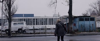 Movie still from “4 Months, 3 Weeks and 2 Days” (2007), directed by Cristian Mungiu – A woman walking down the street in front of a building; Extreme Wide shot, Low angle