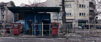 Movie still from “4 Months, 3 Weeks and 2 Days” (2007), directed by Cristian Mungiu – Two people standing in front of a red bus; Wide shot, Over the shoulder angle