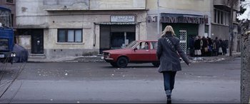 Movie still from “4 Months, 3 Weeks and 2 Days” (2007), directed by Cristian Mungiu – A woman walking down the street in front of a red car; Wide shot, Low angle