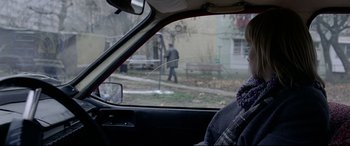 Movie still from “4 Months, 3 Weeks and 2 Days” (2007), directed by Cristian Mungiu – A woman sitting in the driver's seat of a car looking out the window; Close Up shot, Over the shoulder angle