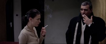 Movie still from “4 Months, 3 Weeks and 2 Days” (2007), directed by Cristian Mungiu – A woman smoking a cigarette while a man stands next to her; Medium shot, Over the shoulder angle