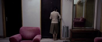 Movie still from “4 Months, 3 Weeks and 2 Days” (2007), directed by Cristian Mungiu – A woman standing in front of an open door in a living room; Wide shot, High angle