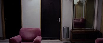 Movie still from “4 Months, 3 Weeks and 2 Days” (2007), directed by Cristian Mungiu – A room with a pink couch and a black door; Wide shot, High angle