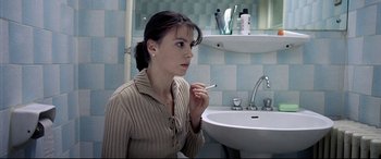 Movie still from “4 Months, 3 Weeks and 2 Days” (2007), directed by Cristian Mungiu – A woman sitting in front of a bathroom sink holding a cigarette; Close Up shot, Over the shoulder angle