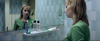 Movie still from “4 Months, 3 Weeks and 2 Days” (2007), directed by Cristian Mungiu – A woman sitting in front of a bathroom mirror in front of a sink; Medium shot, Over the shoulder angle