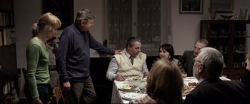 Movie still from “4 Months, 3 Weeks and 2 Days” (2007), directed by Cristian Mungiu – A group of people sitting at a table with plates of food on it; Medium shot, Over the shoulder angle