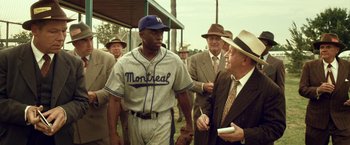 Movie still from “42” (2013), directed by Brian Helgeland – A group of men standing next to each other on top of a baseball field; Medium shot, Over the shoulder angle
