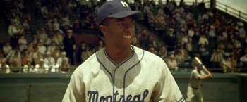 Movie still from “42” (2013), directed by Brian Helgeland – A baseball player smiling for the camera in a stadium; Medium shot, Over the shoulder angle