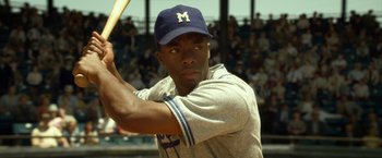 Movie still from “42” (2013), directed by Brian Helgeland – A baseball player holding a baseball bat on top of a baseball field; Medium shot, Over the shoulder angle