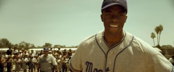 Movie still from “42” (2013), directed by Brian Helgeland – A man in a baseball uniform smiling for the camera; Close Up shot, Over the shoulder angle