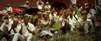 Movie still from “42” (2013), directed by Brian Helgeland – A group of people sitting in the grass holding umbrellas; Extreme Wide shot, High angle