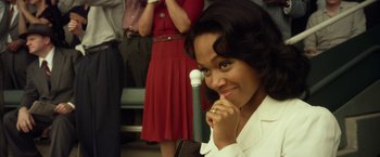 Movie still from “42” (2013), directed by Brian Helgeland – A woman in a white shirt is holding a microphone and smiling; Close Up shot, Over the shoulder angle