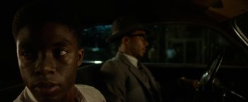 Movie still from “42” (2013), directed by Brian Helgeland – A man in a suit and hat sitting in the back of a car; Close Up shot, Over the shoulder angle