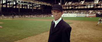 Movie still from “42” (2013), directed by Brian Helgeland – A man in a black suit and a black hat stands on a baseball field; Medium shot, High angle