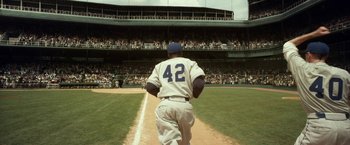 Movie still from “42” (2013), directed by Brian Helgeland – A baseball player walking on a baseball field; Wide shot, Low angle