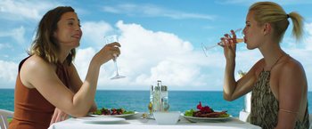 Movie still from “47 Meters Down” (2017), directed by Johannes Roberts – A person holding a wine glass over a plate of food on a table; Medium shot, Low angle