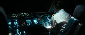 Movie still from “7500” (2019), directed by Patrick Vollrath – A man wearing headphones sitting in an airplane cockpit at night; Medium shot, High angle