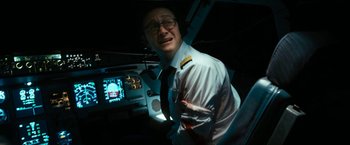 Movie still from “7500” (2019), directed by Patrick Vollrath – A man wearing a uniform and glasses in a dark room; Medium shot, High angle