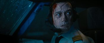 Movie still from “7500” (2019), directed by Patrick Vollrath – A man in a white shirt and headphones with blood all over his face; Close Up shot, Overhead angle