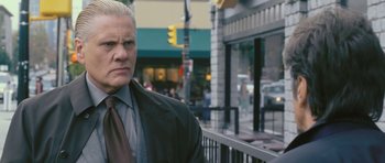 Movie still from “88 Minutes” (2007), directed by Jon Avnet – A man standing on the sidewalk in front of a building; Close Up shot, Over the shoulder angle