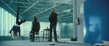 Movie still from “88 Minutes” (2007), directed by Jon Avnet – A woman standing next to a chair in a room; Wide shot, Low angle