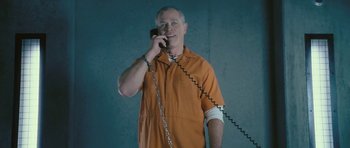 Movie still from “88 Minutes” (2007), directed by Jon Avnet – A man in an orange prison uniform talking on a phone; Medium shot, Low angle