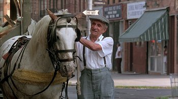 Movie still from “A Bronx Tale” (1993), directed by Robert De Niro – An old man standing next to a white horse on a city street; Medium shot, Low angle