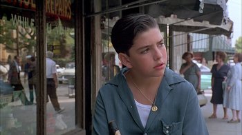 Movie still from “A Bronx Tale” (1993), directed by Robert De Niro – A young man with a beard is standing on the sidewalk; Close Up shot, Low angle
