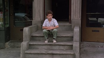 Movie still from “A Bronx Tale” (1993), directed by Robert De Niro – A young boy sitting on the steps of a building; Wide shot, High angle