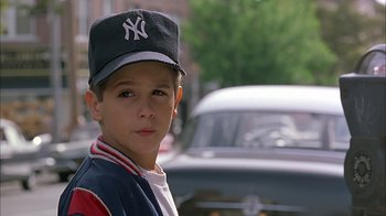 Movie still from “A Bronx Tale” (1993), directed by Robert De Niro – A young boy wearing a baseball cap in front of a parked car; Close Up shot, Low angle