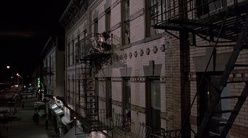 Movie still from “A Bronx Tale” (1993), directed by Robert De Niro – A fire escape on the side of a brick building at night; Extreme Wide shot, Low angle
