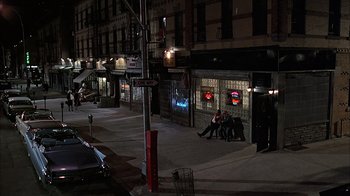 Movie still from “A Bronx Tale” (1993), directed by Robert De Niro – A group of people sitting on a sidewalk at night; Extreme Wide shot, High angle
