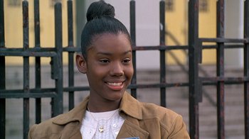 Movie still from “A Bronx Tale” (1993), directed by Robert De Niro – A young woman smiles while standing in front of a fence; Close Up shot, Low angle