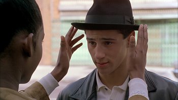 A young man wearing a hat is touching the ear of another young man