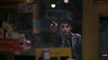 Movie still from “A Bronx Tale” (1993), directed by Robert De Niro – A man in a black hat and leather jacket holding a camera; Medium shot, Over the shoulder angle
