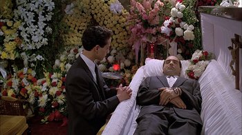 Movie still from “A Bronx Tale” (1993), directed by Robert De Niro – A man in a suit and tie sitting next to another man in a suit and tie in front of flowers; Medium shot, High angle