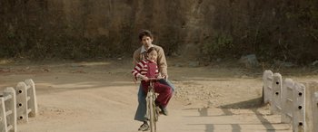 Movie still from “A Death in the Gunj” (2016), directed by Konkona Sen Sharma – A man and a child riding a bike on a dirt road; Medium shot, High angle