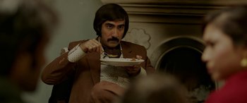 Movie still from “A Death in the Gunj” (2016), directed by Konkona Sen Sharma – A man in a brown suit eating a piece of cake; Medium shot, Over the shoulder angle